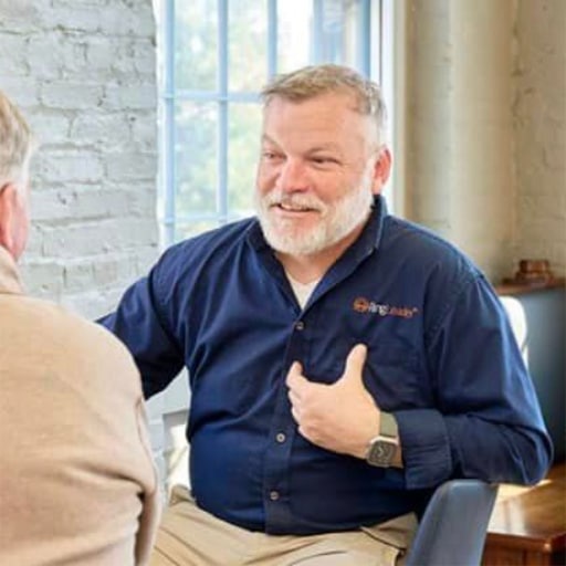 The image features a professional conversation taking place at RingSpaces Coworking in Fredericksburg. One individual, identified as Neil Darling, the owner of RingSpaces, is engaging warmly with another person. The setting reflects a collaborative and approachable environment, characteristic of the coworking space.